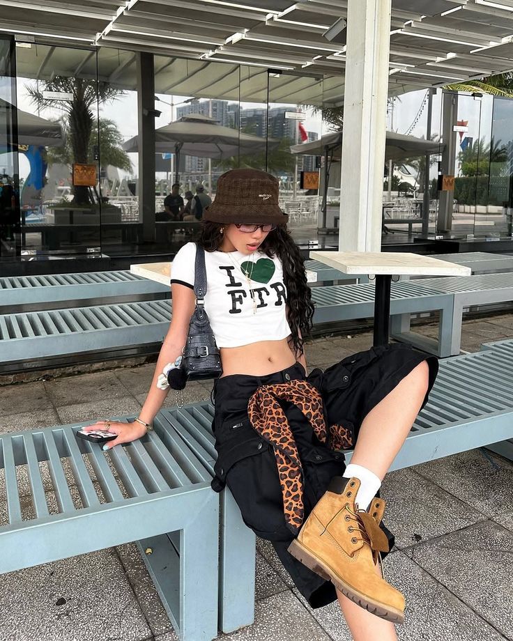 Woman in a crop top, cargo pants, and bucket hat sitting outdoors