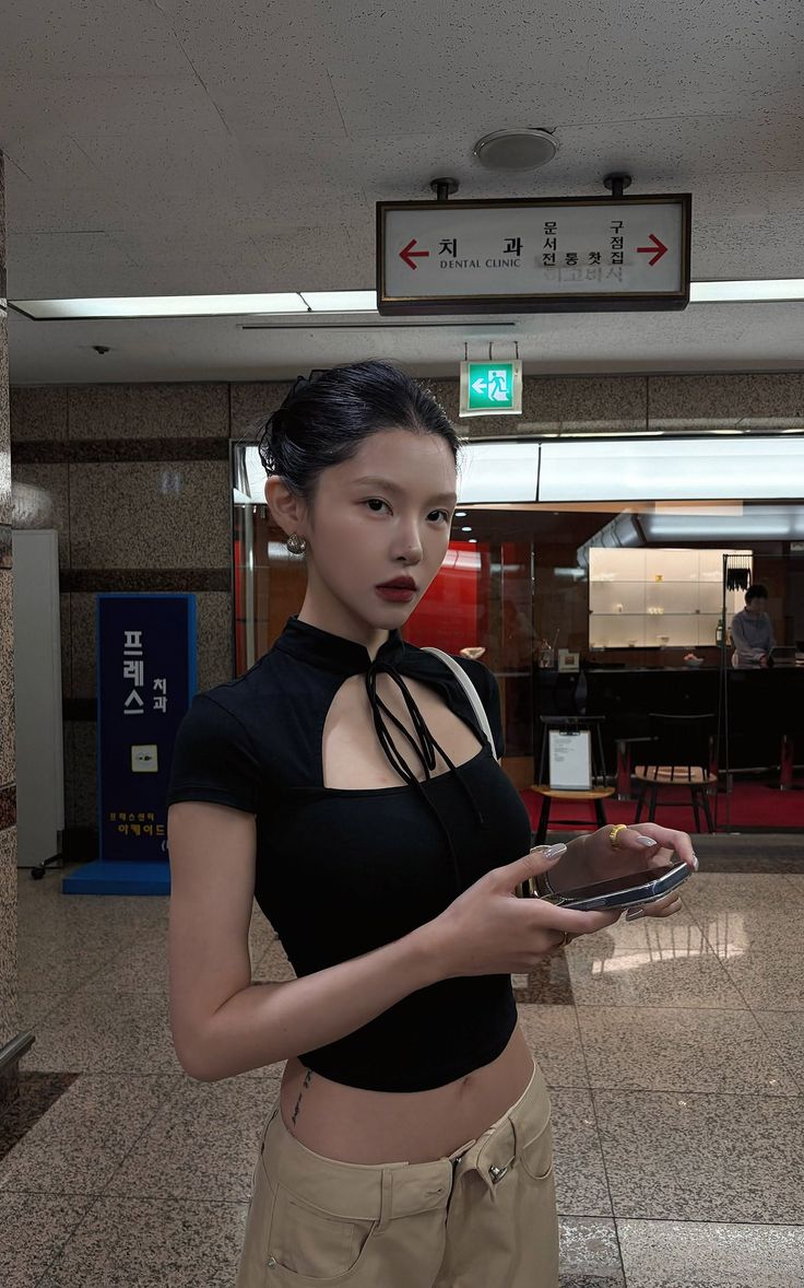 Woman in a black top and beige pants holding a phone indoors