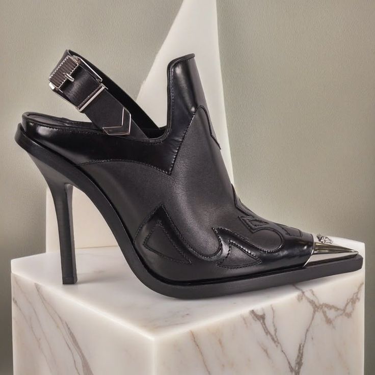 Black leather high-heel slingback shoe with western-style detailing on a marble pedestal