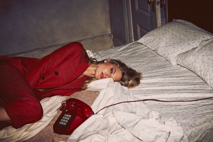Woman in a red suit lying on a bed with a vintage red phone