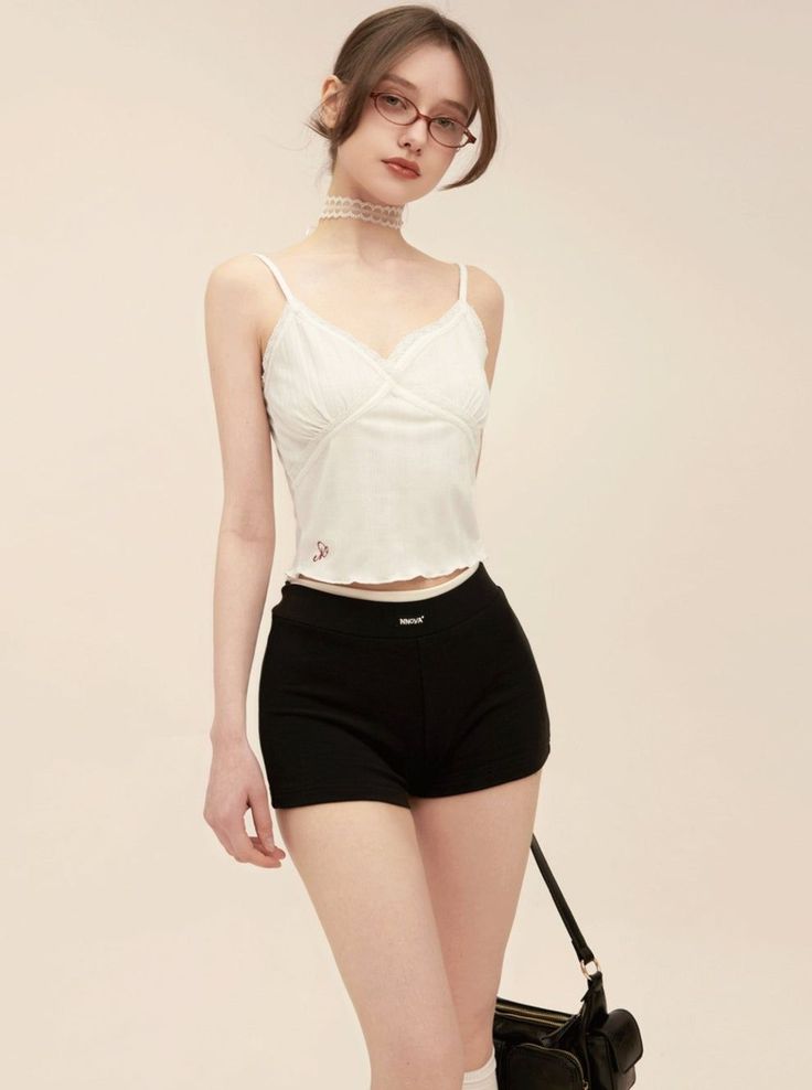 Woman in a white camisole and black shorts with an updo and glasses