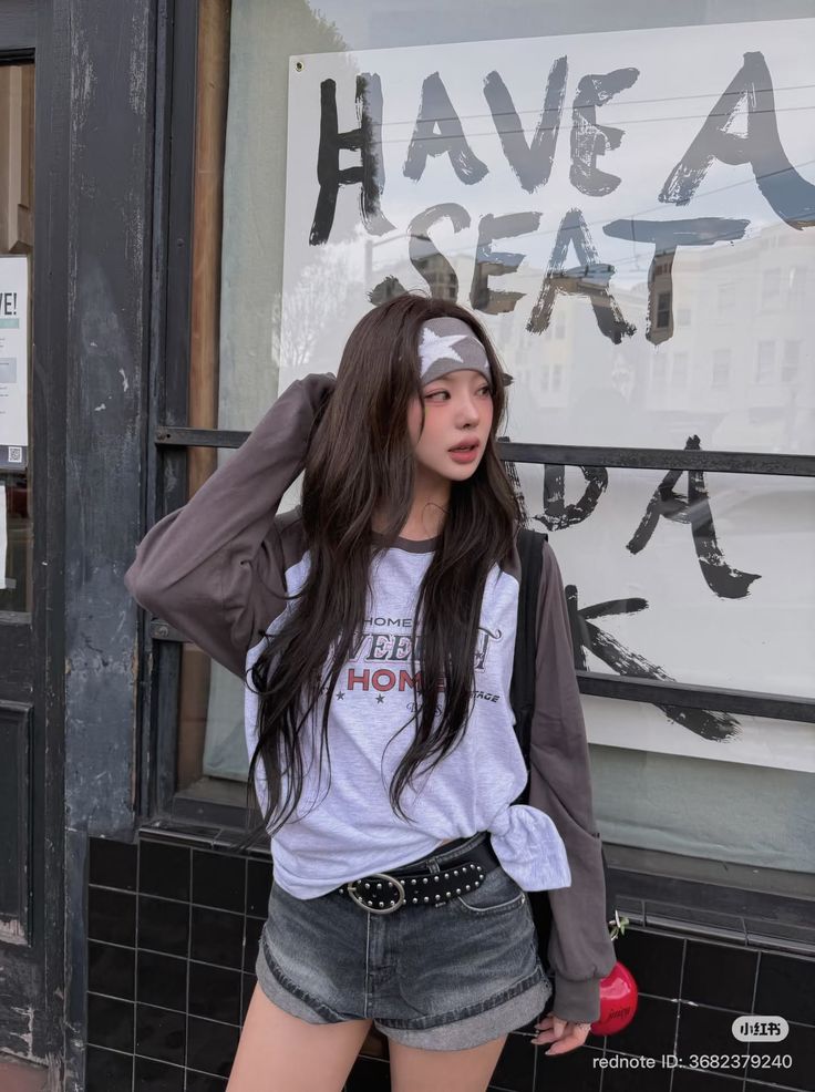 Woman with long hair and a headband wearing denim shorts and a long sleeve shirt outdoors
