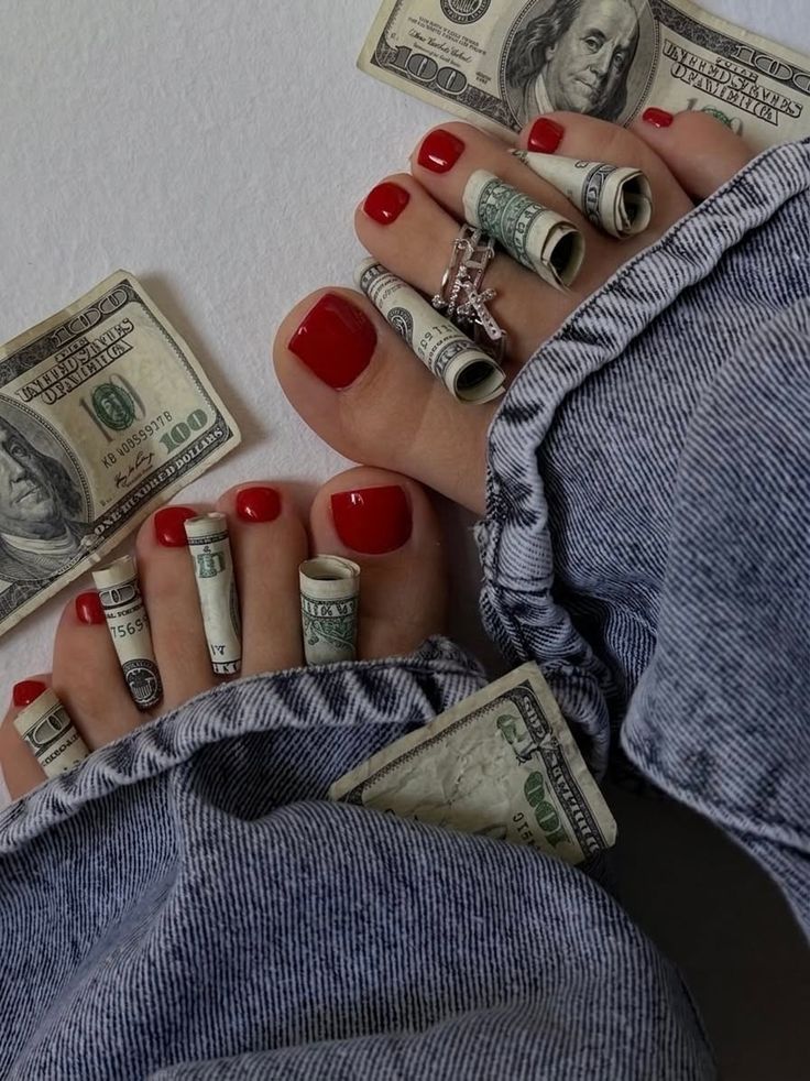 Feet with red nail polish and rolled dollar bills between toes