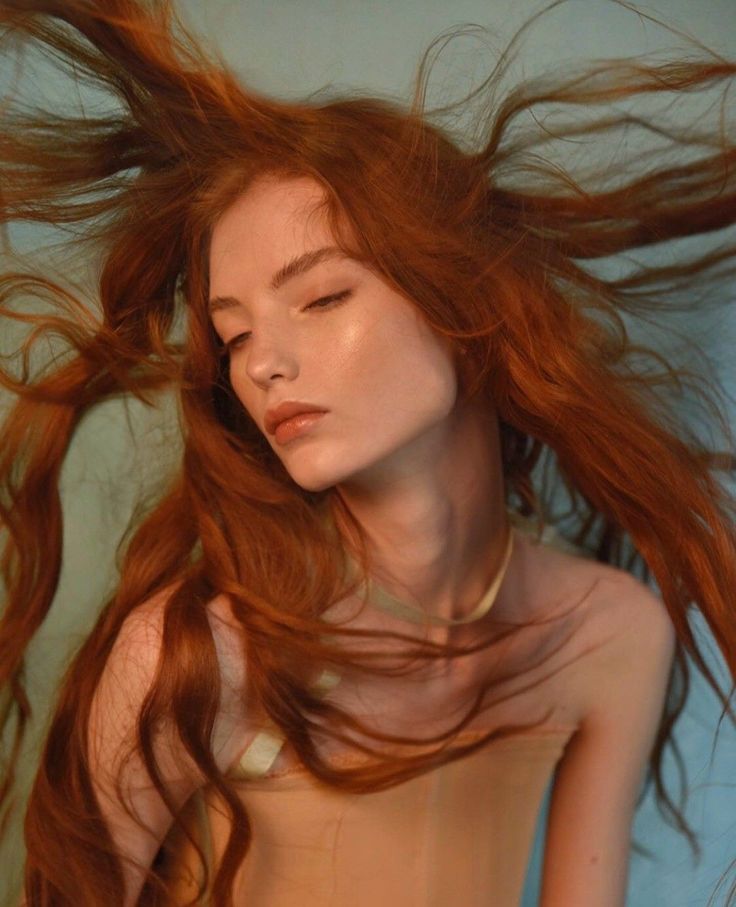 Woman with long red hair and closed eyes, wearing a strapless top