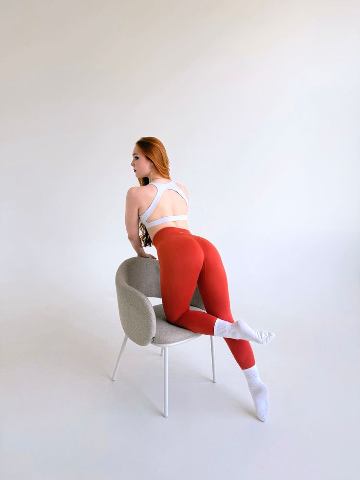 Woman with red hair in a sports bra and red leggings posing on a chair