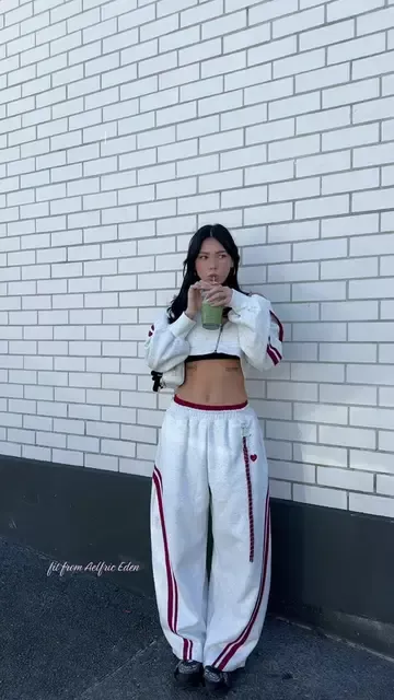Woman in a white crop top and sweatpants drinking from a cup outdoors