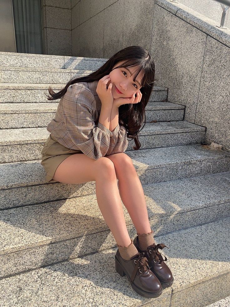 Woman with long hair sitting on outdoor stairs in a plaid shirt and mini skirt