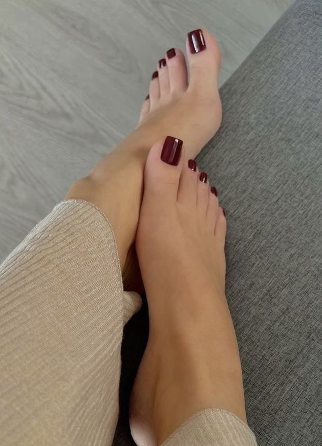 Close up of bare feet with red nail polish, crossed on a gray surface