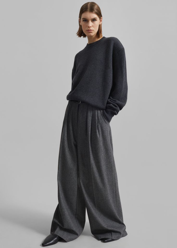 Woman in a dark grey sweater and wide leg pants posing in a studio