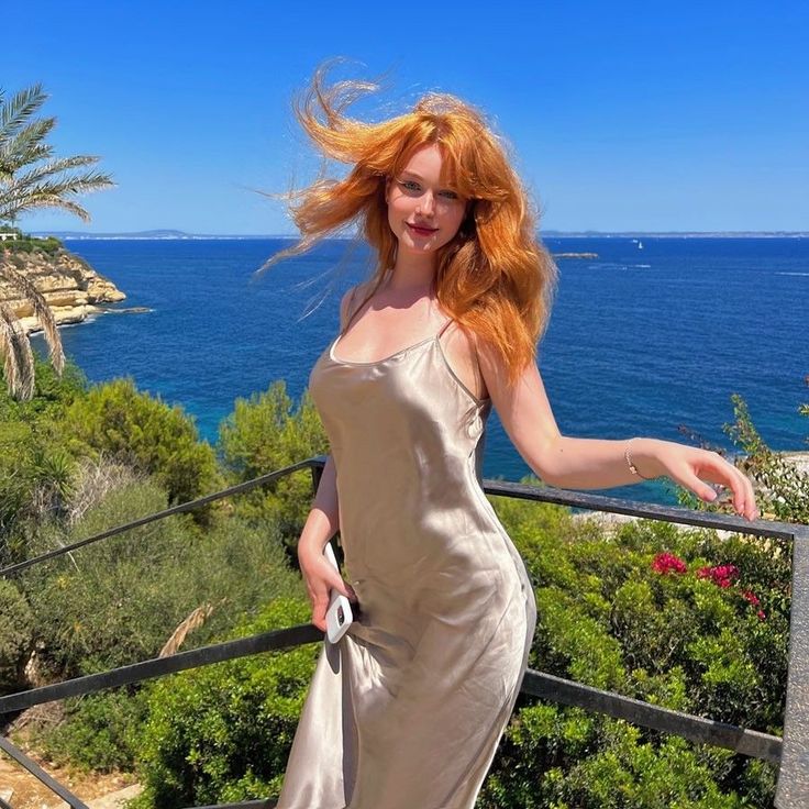 Woman with red hair in a slip dress on a balcony overlooking the ocean