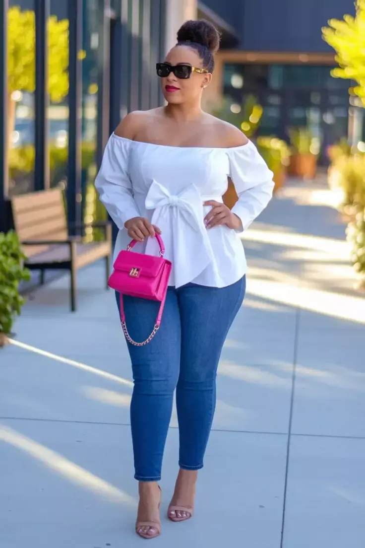 Woman in an off-shoulder top, blue jeans, and a pink handbag outdoors
