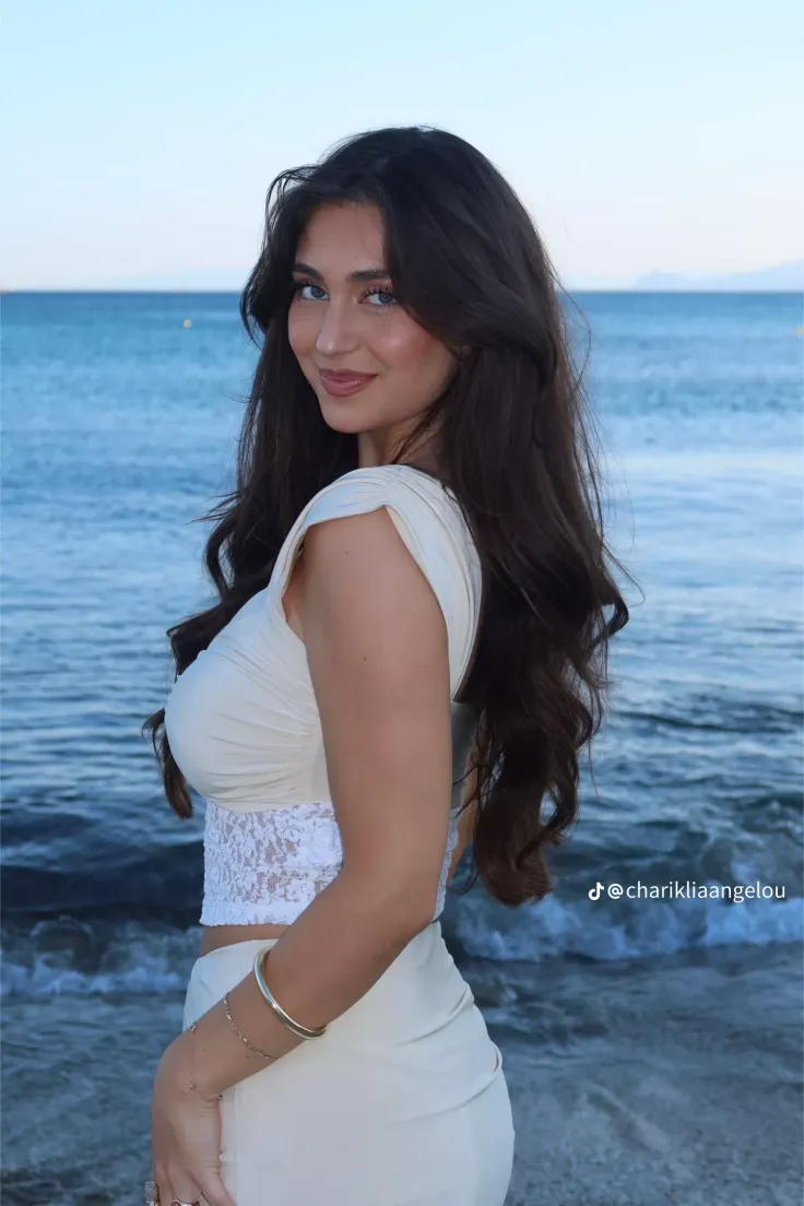 Woman with long dark hair wearing a white top with lace trim at the beach