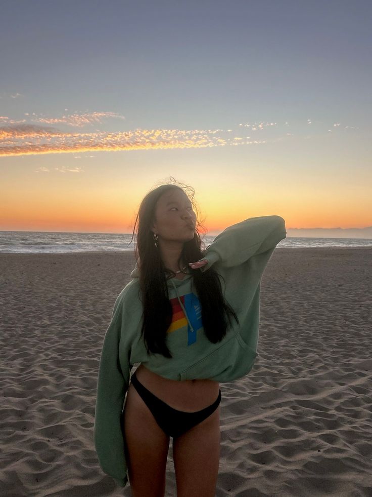 Woman in a hoodie and bikini bottoms on a beach at sunset