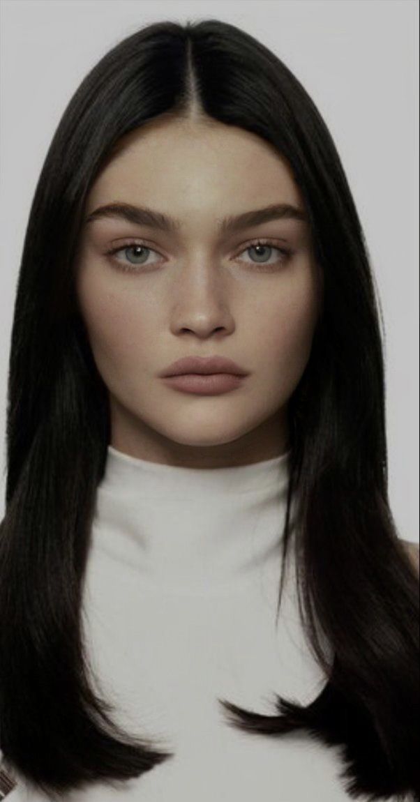 Woman with long black hair wearing a white turtleneck in a studio portrait