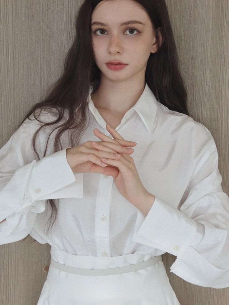 Woman with long dark hair wearing a white shirt, hands clasped in front