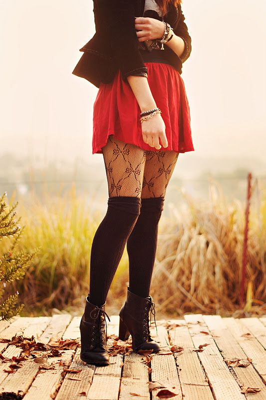 Person in a red skirt and patterned tights standing on a wooden path with autumn leaves