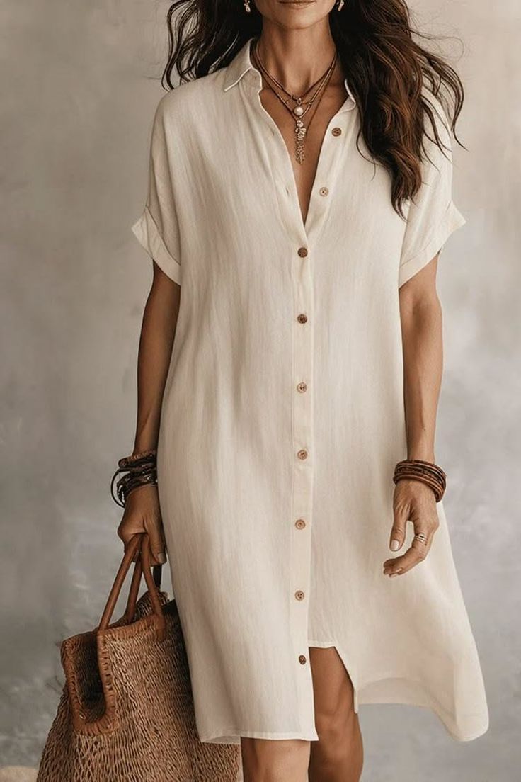 Woman in a light shirt dress holding a straw bag with layered necklaces and bracelets