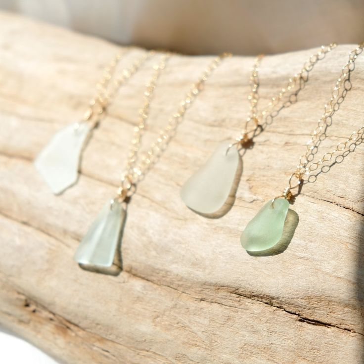 Sea glass necklaces with gold chains displayed on driftwood