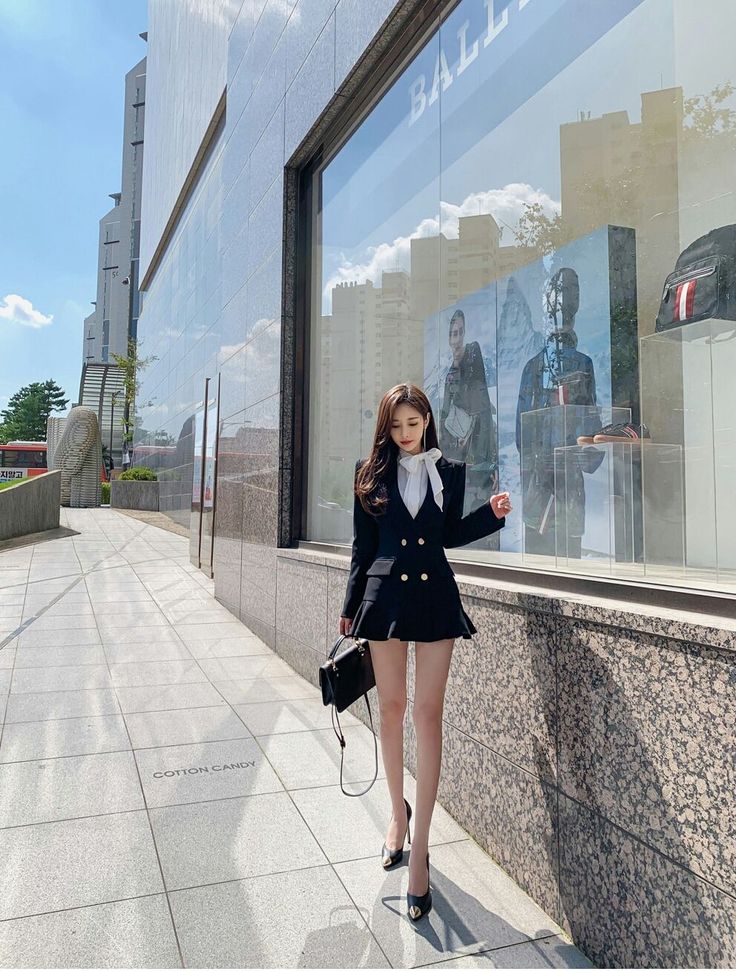 Woman in a black blazer dress and white bow blouse walking on a city street