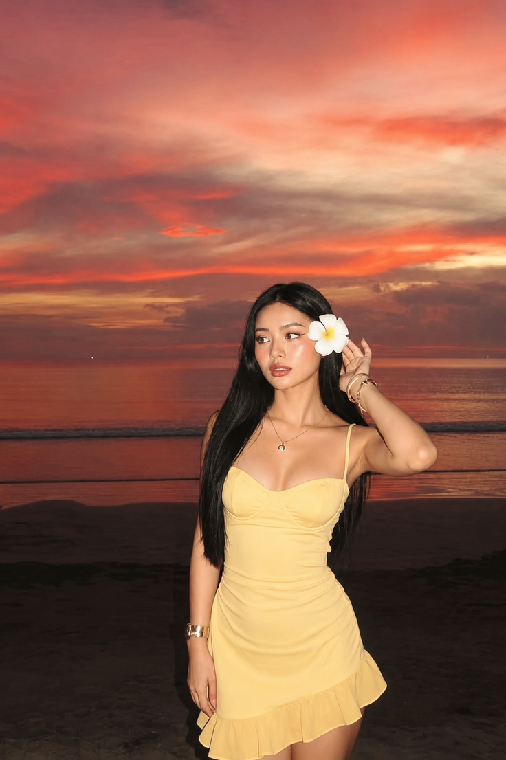 Woman in a yellow dress with a frangipani flower in her hair at sunset on a beach