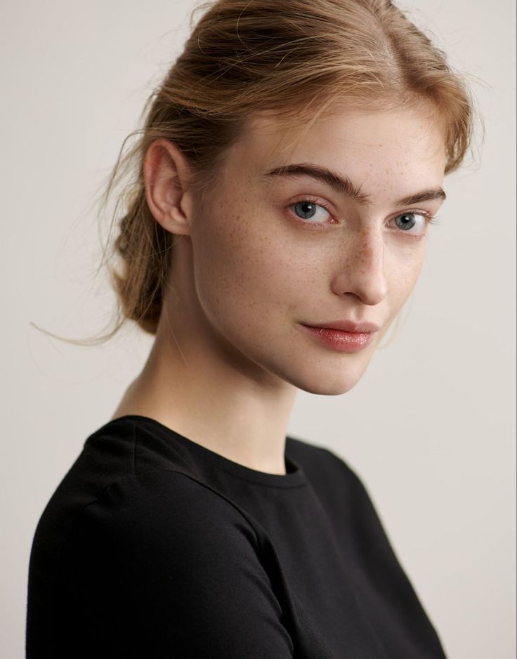 Woman with blonde hair and freckles wearing a black shirt, looking at the camera