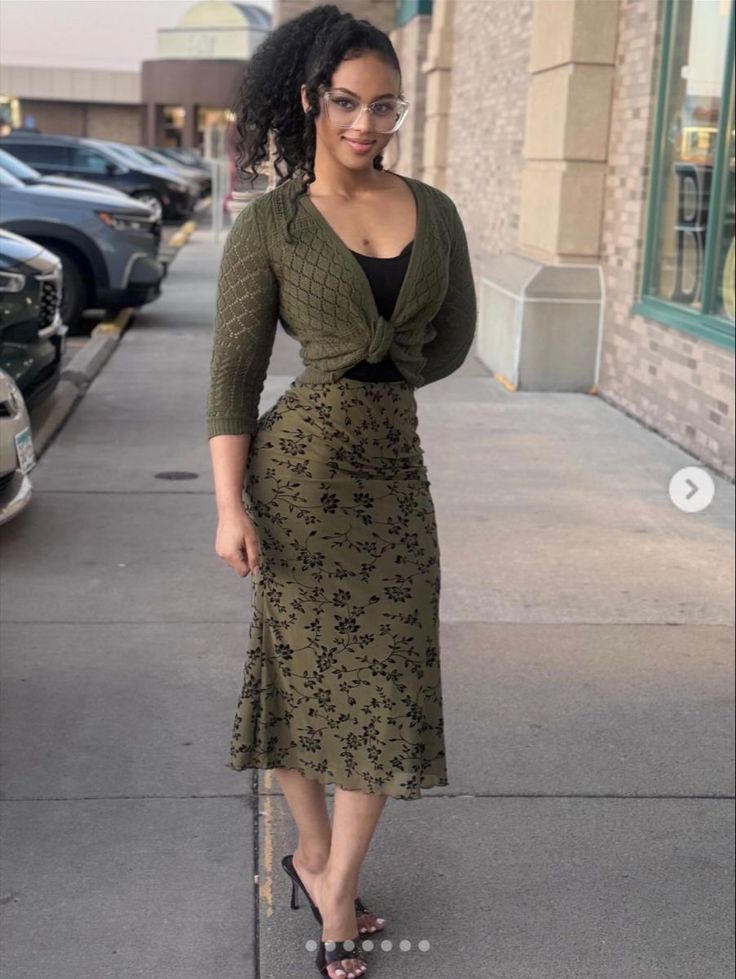 Woman with curly ponytail and glasses wearing a green floral skirt and cardigan