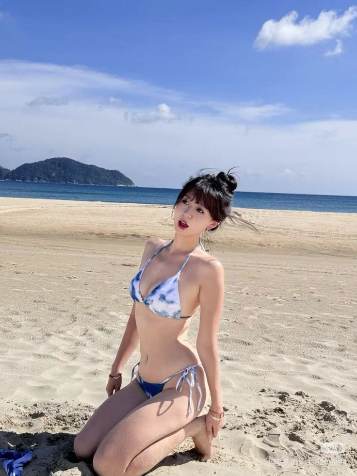 Woman in a blue and white bikini kneeling on a sandy beach