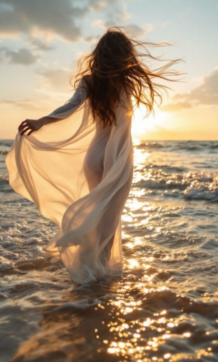 Woman in a sheer dress walking in the ocean at sunset