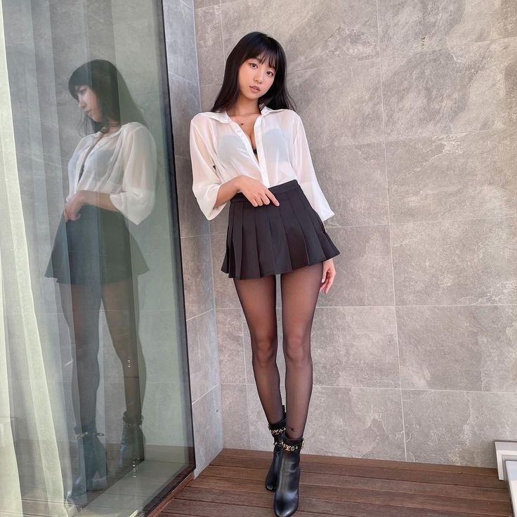 Woman in a white shirt and black pleated skirt with tights and ankle boots