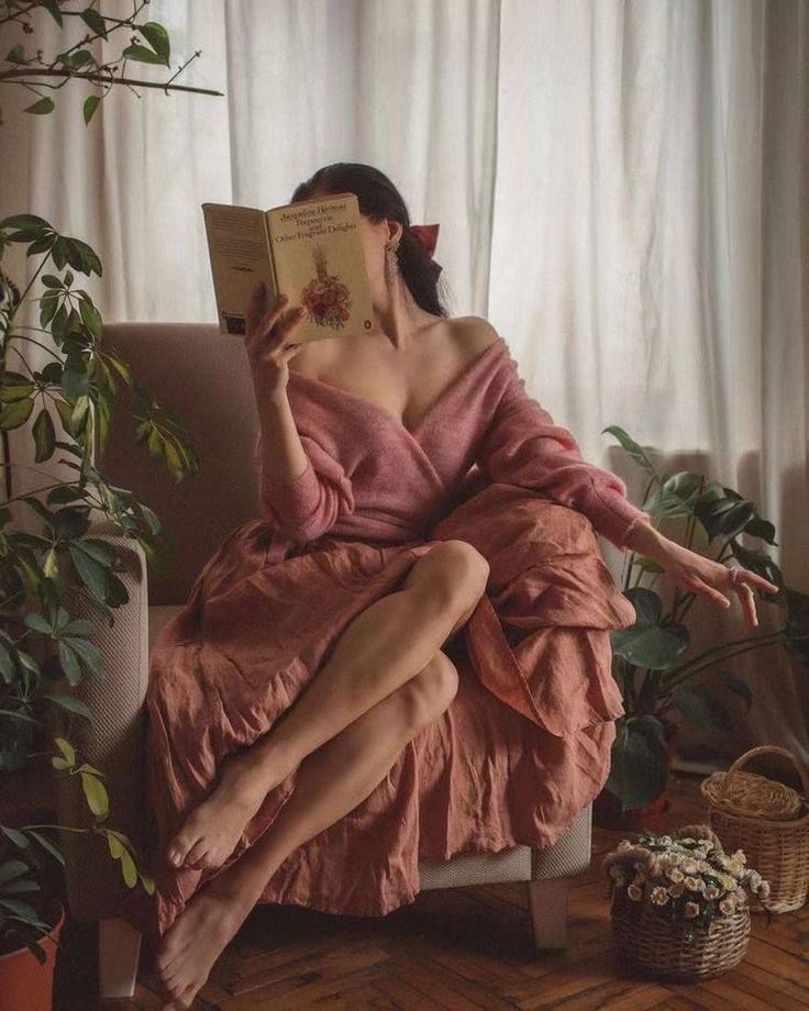 Woman in a pink dress reading a book indoors with plants