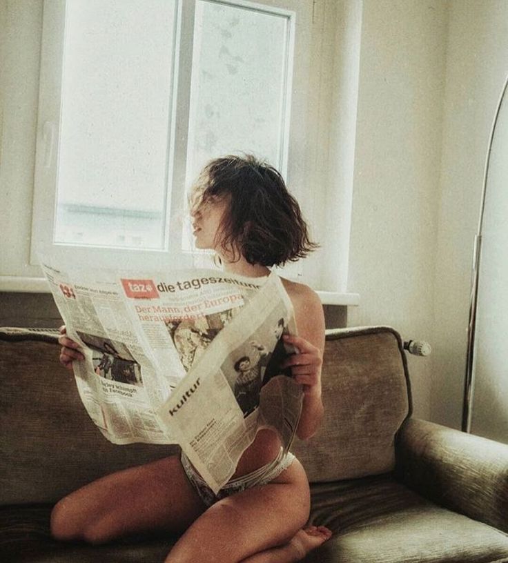 Woman in underwear reading a newspaper on a couch indoors