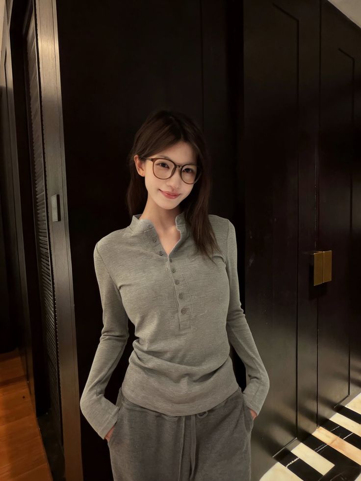 Woman with long hair and glasses wearing a gray shirt and sweatpants indoors